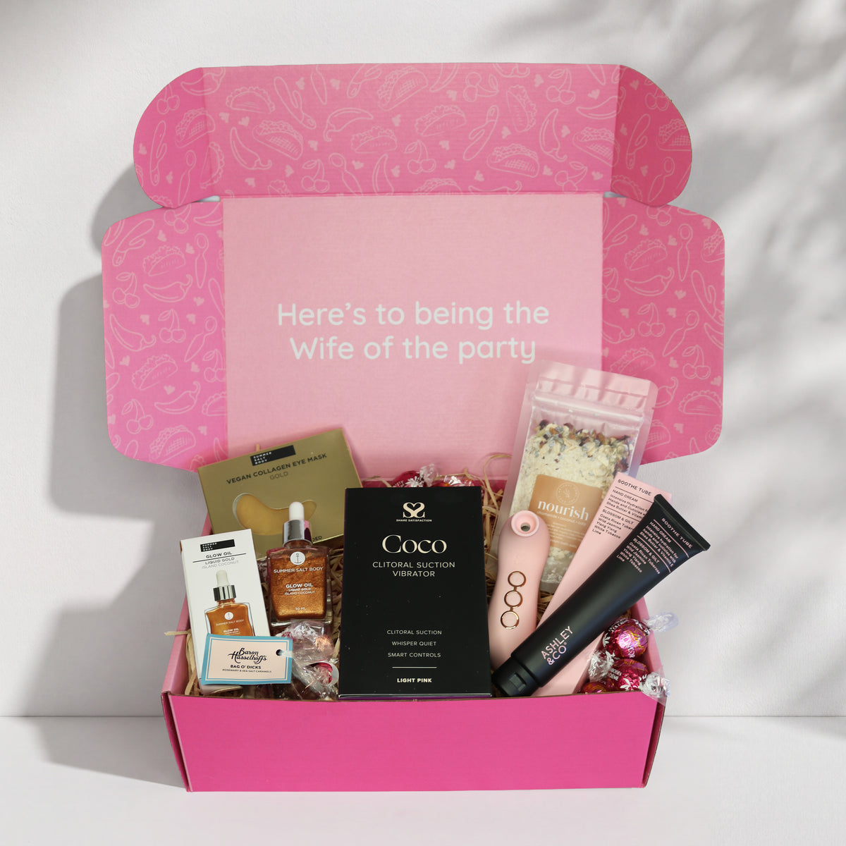 Bridal self-love gift box -Pink box with 'Here's to being the wife of the party' text, surrounded by various pamper products + pleasure toy. Happy Pink Taco, New Zealand.