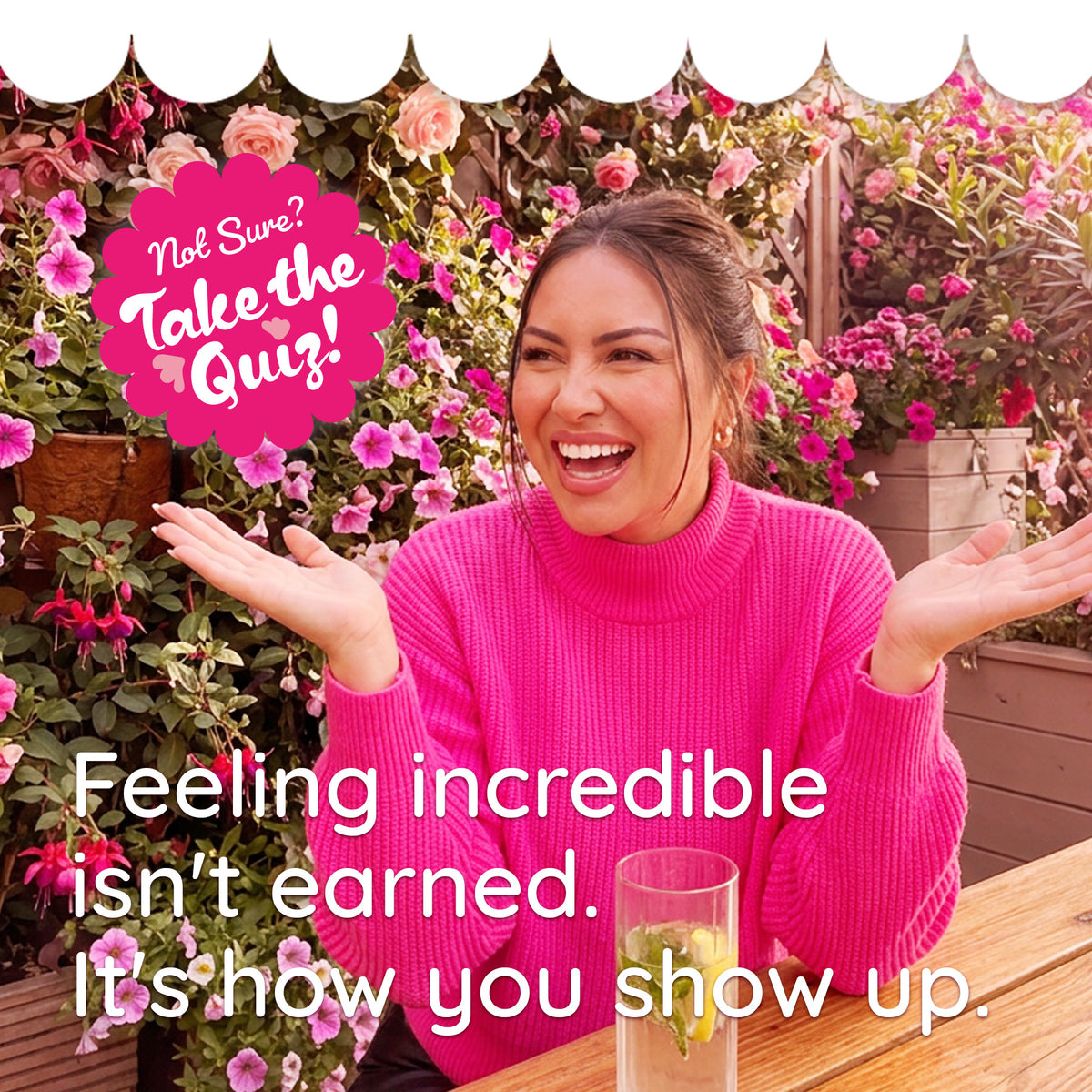 A smiling woman in a bright pink turtleneck sweater sits outdoors at a wooden table with flowers behind her. Large white text reads 'Feeling incredible isn't earned.