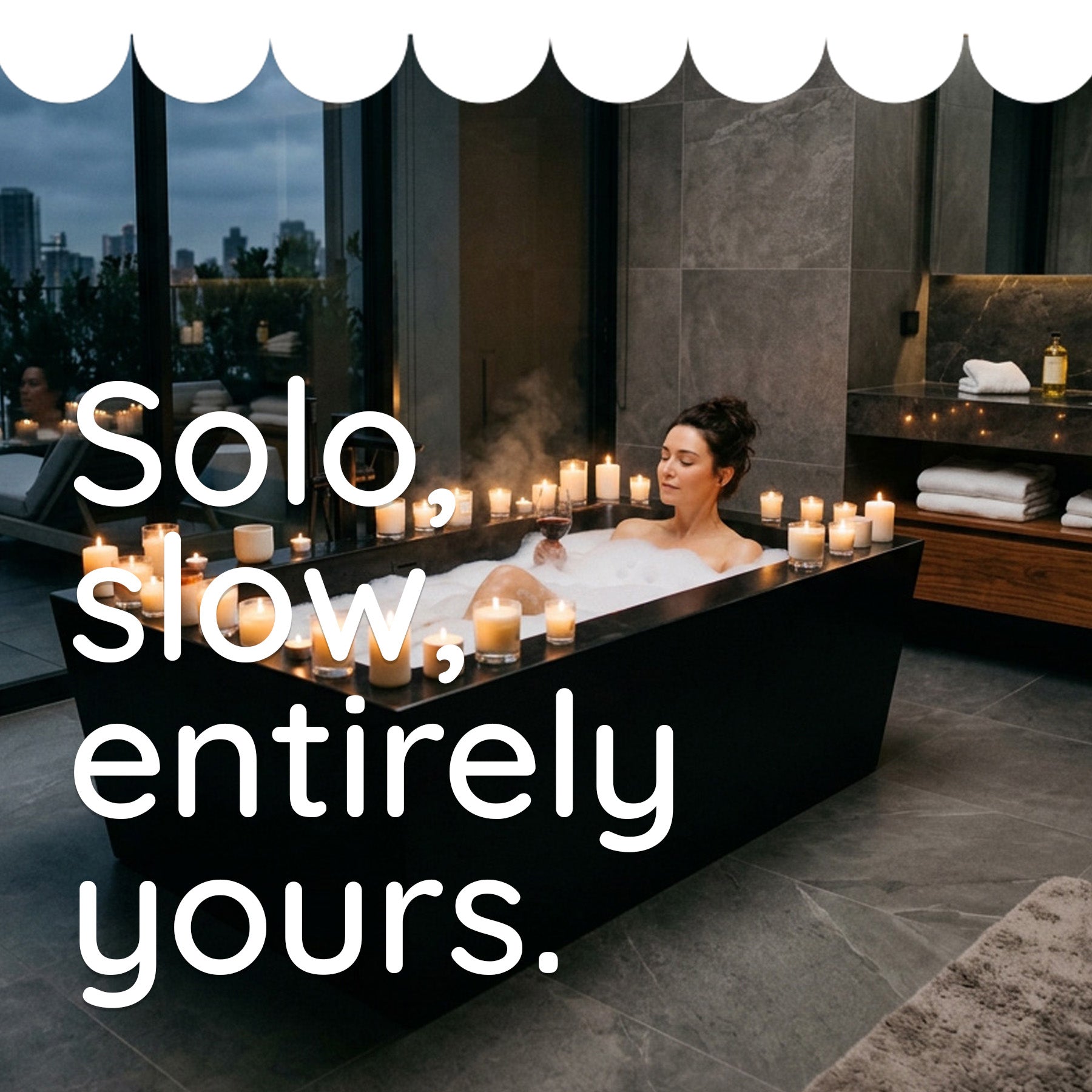 A woman relaxes in a bubble bath set with many lit candles in a modern bathroom. Large white text overlays the left side reading, 'Solo, slow, entirely yours.