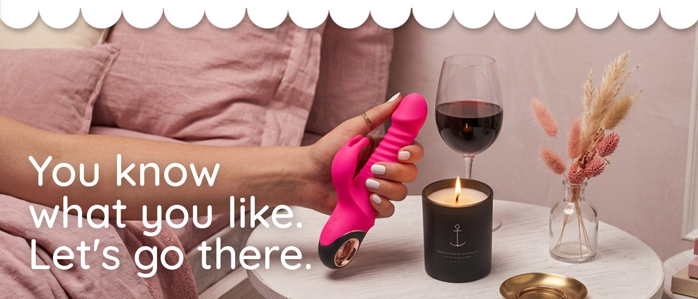 A hand holds a bright pink personal massager with a metallic base in a bedroom setting next to a glass of red wine, a lit candle, and a vase with dried grasses. Text on the left reads, 'You know what you like.